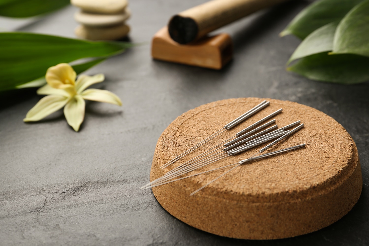 Cork coaster with acupuncture needles on black table. Space for text